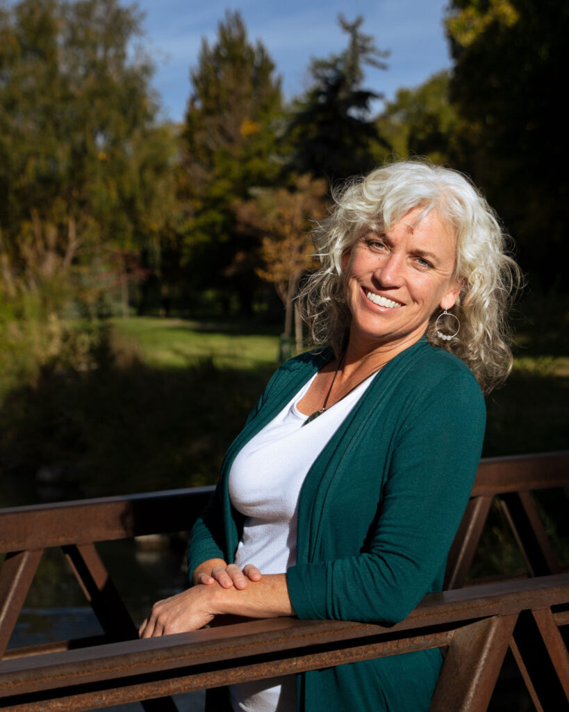 Dr. Leslie Peterson, N.D., smiling outdoors beside a park footbridge