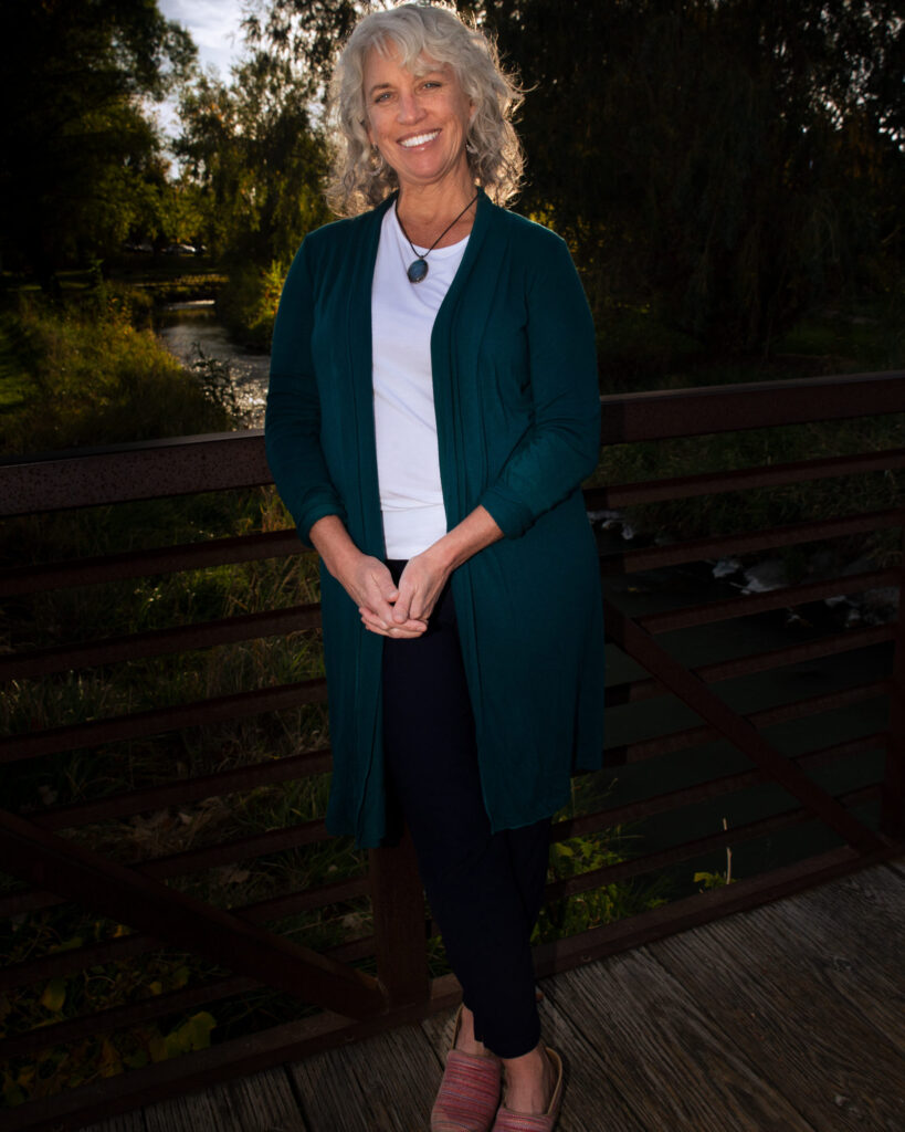 Dr. Leslie Peterson, N.D., smiling on a wooden footbridge over a creek.