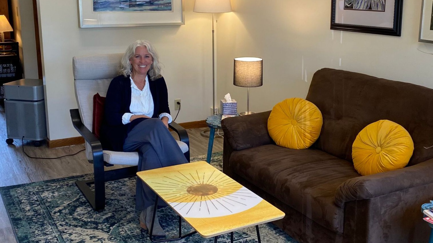 Dr. Peterson seated in an armchair in the front room of the Full Circle Care office, beside a couch with round yellow cushions.